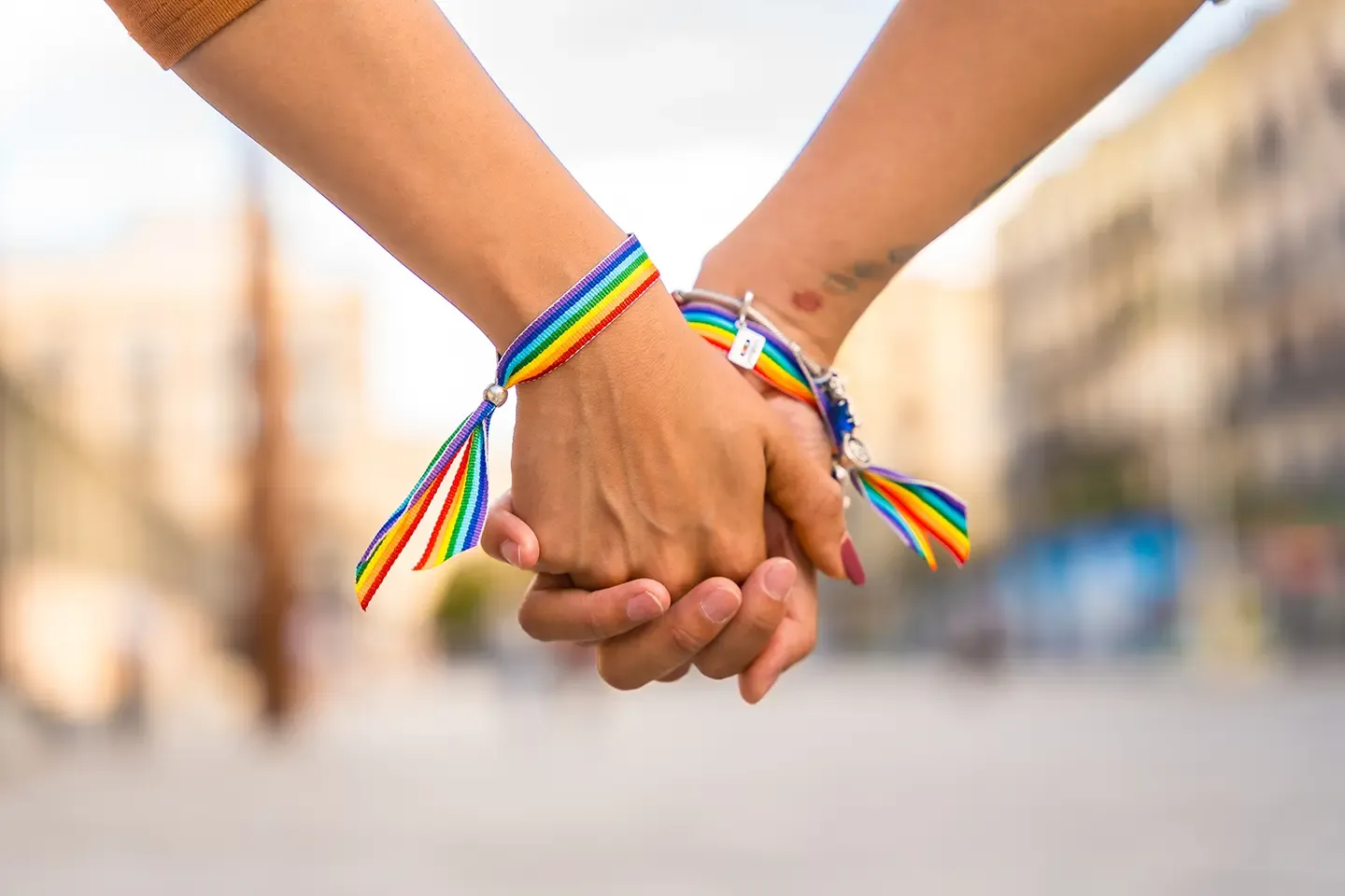 Two hands holding with rainbow bracelets
